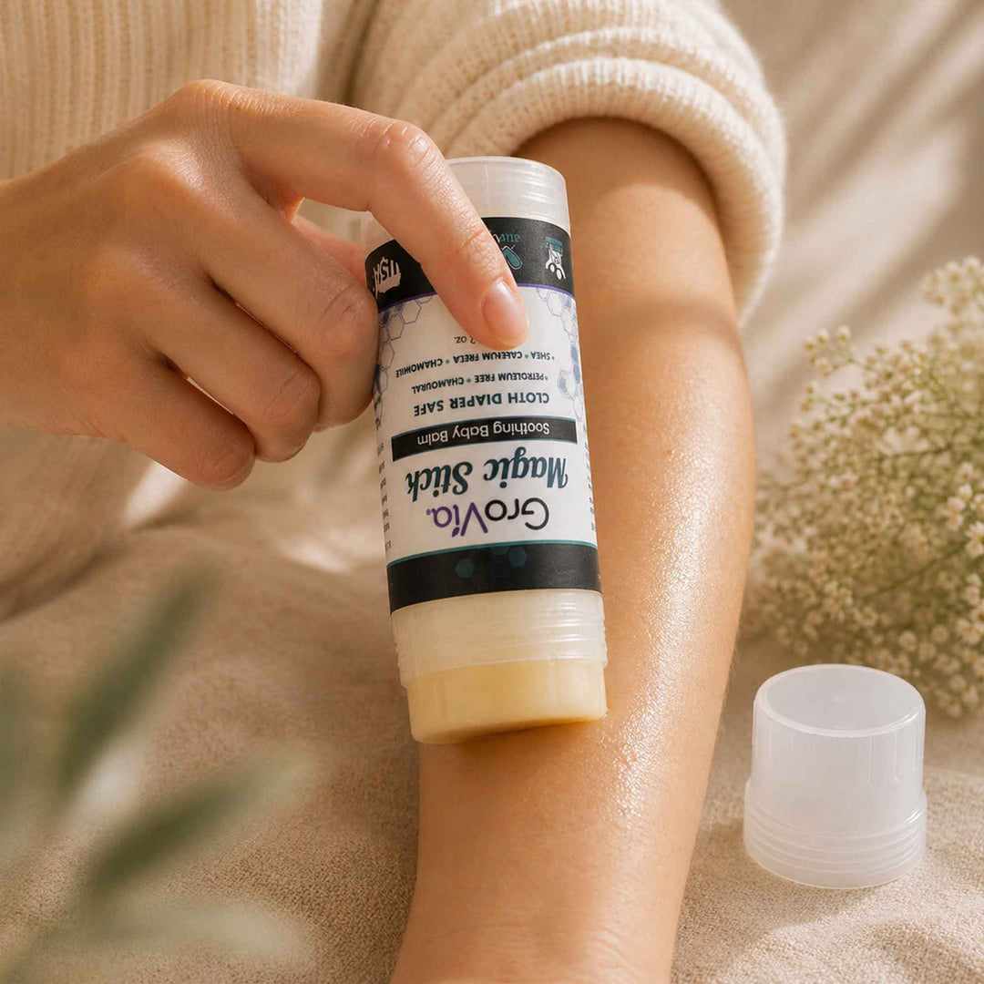 Person applying a stick of Magic Stick soothing baby balm from Grovia on their arm with a blurred natural background.