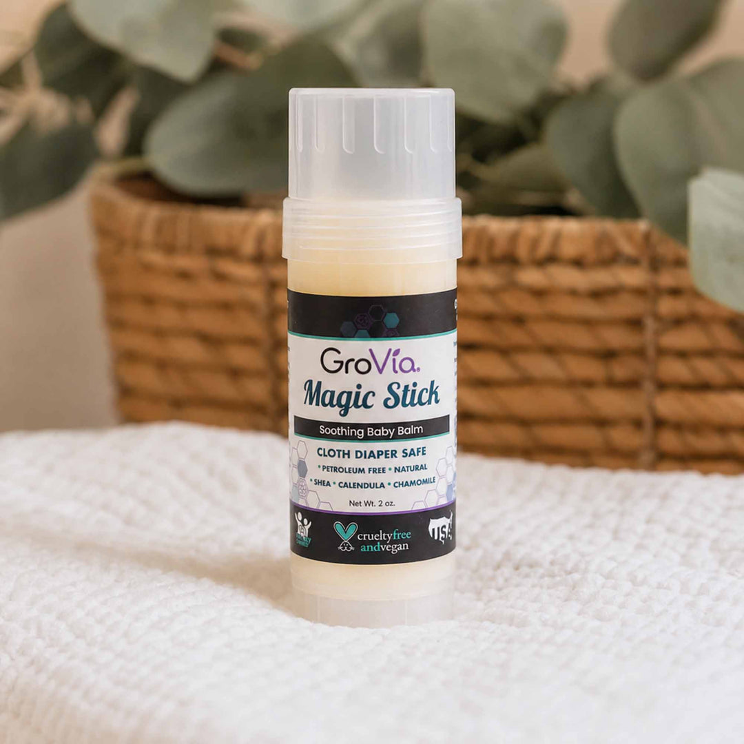 GroVia Magic Stick balm on a textured surface with a blurred plant background