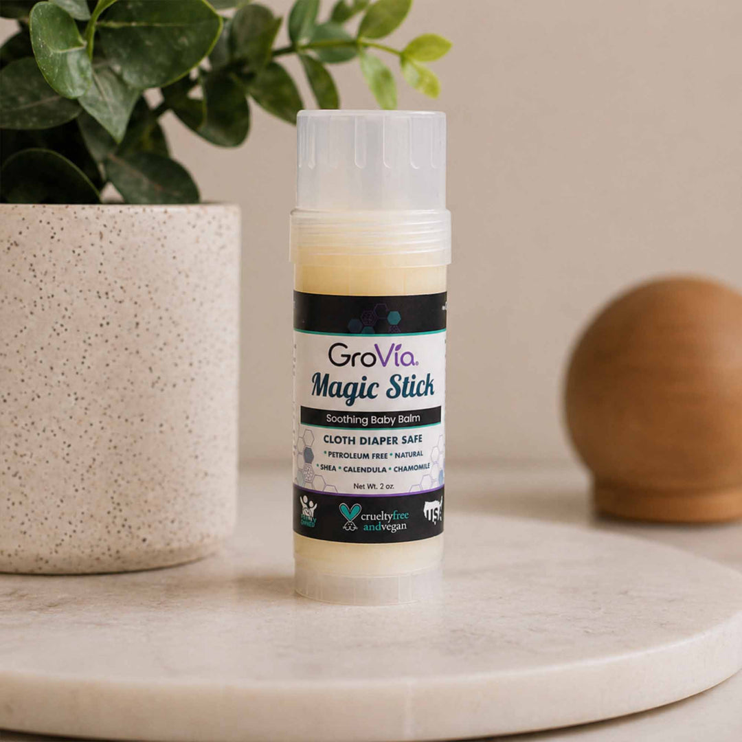 GroVia Magic Stick balm on a surface with a plant and decorative object in the background