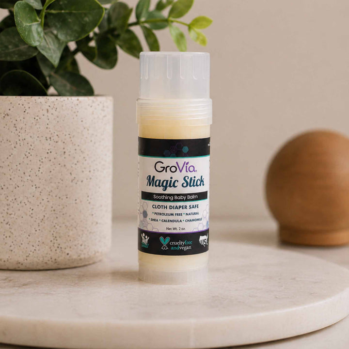 GroVia Magic Stick balm on a surface with a plant and decorative object in the background