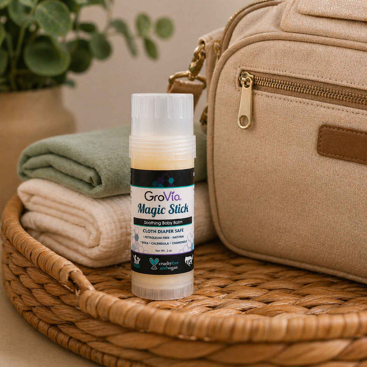GroVia Magic Stick on a woven surface with a beige bag and folded cloths in the background